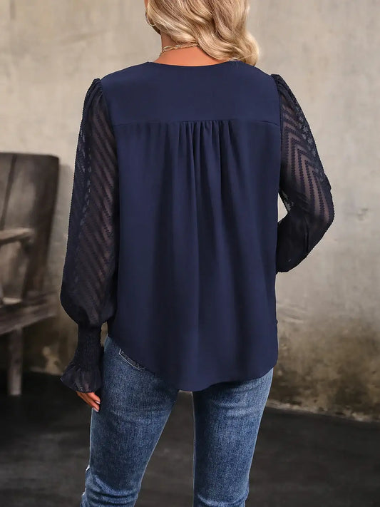 Woman wearing navy blouse with sheer lace long sleeves and blue jeans, standing indoors