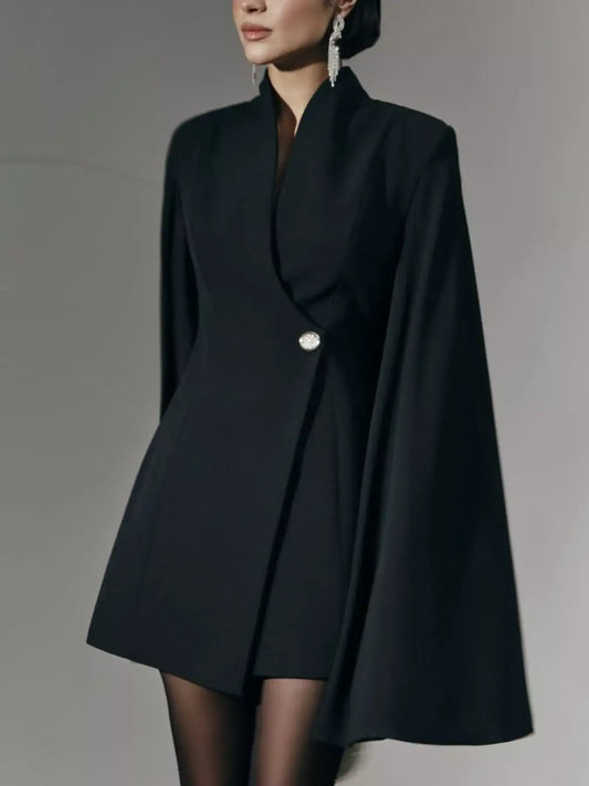 Woman wearing chic black cape blazer dress with single decorative button and statement earrings