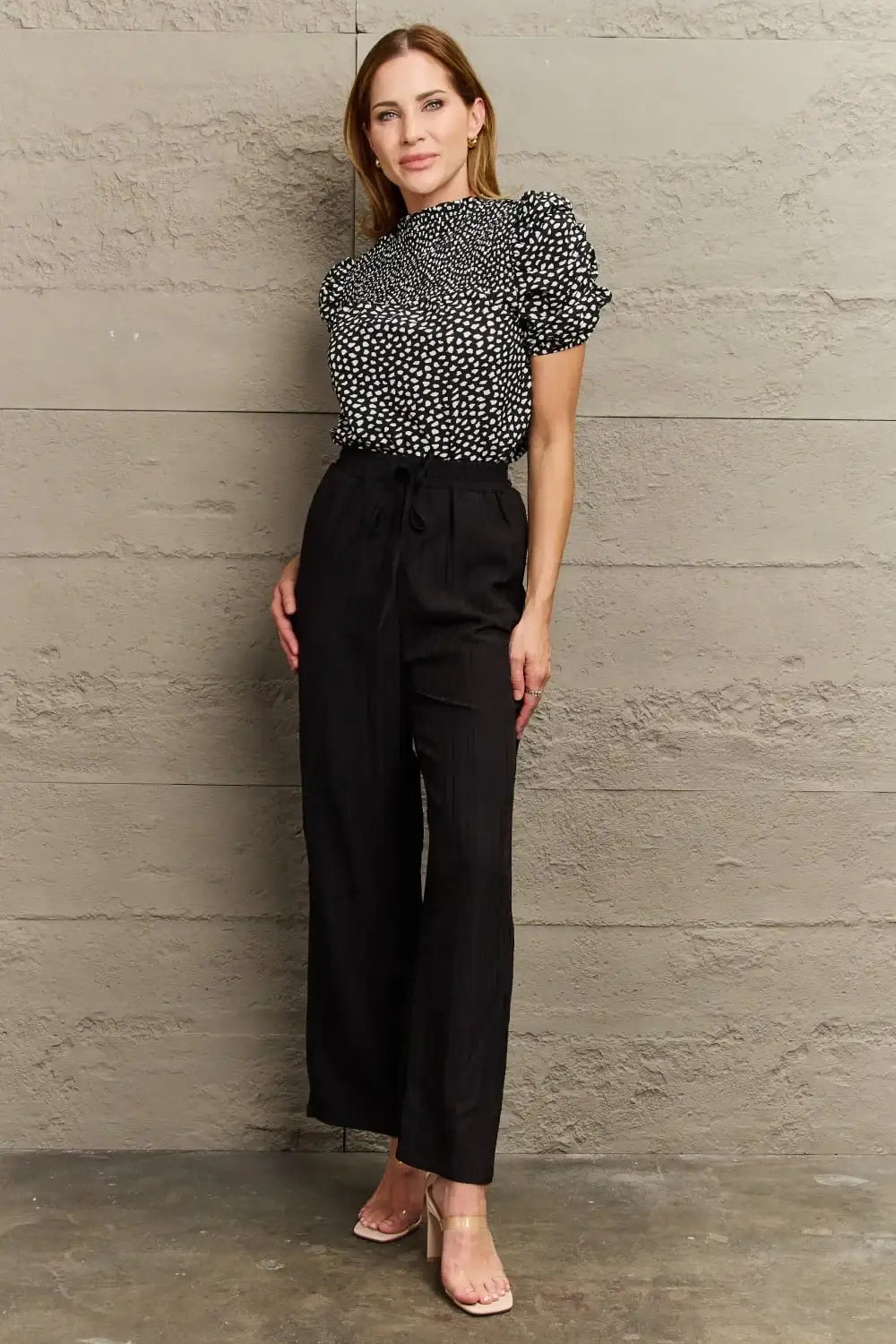 Woman wearing a black and white patterned blouse with short sleeves and high-waisted black pants