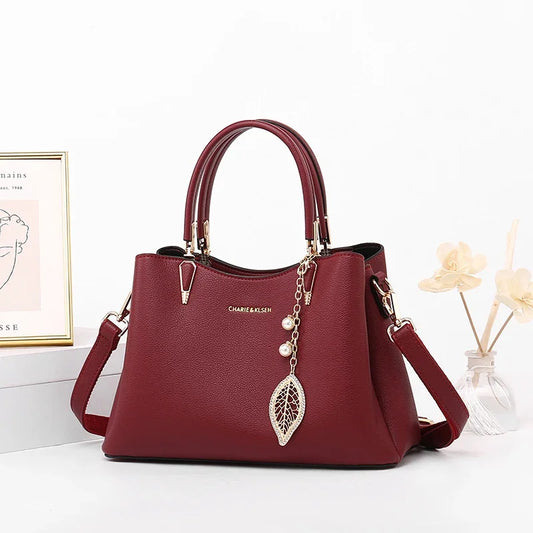 Elegant burgundy leather handbag with gold hardware, leaf and pearl charm, double handles.