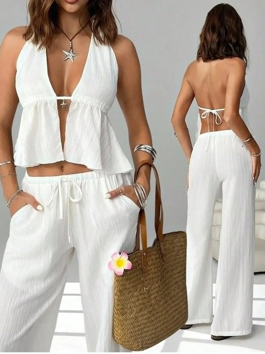 Woman in a white halter top and wide-leg pants set, holding straw tote bag, with boho jewelry.