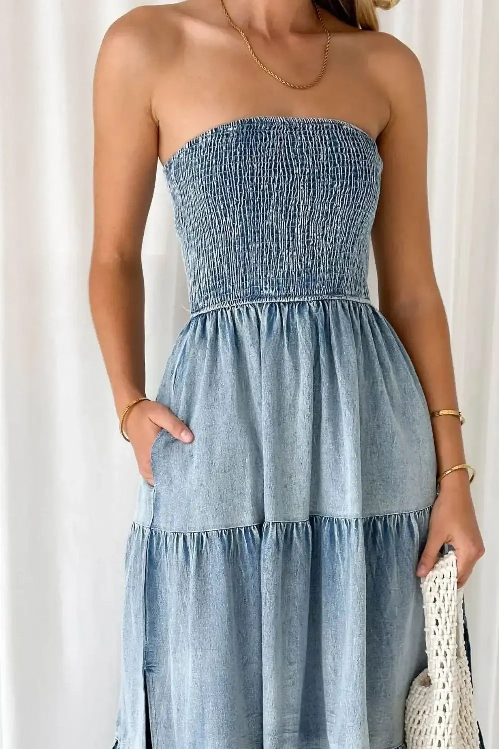 Woman wearing a strapless smocked denim dress with pockets and gold jewelry