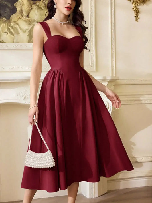 Woman wearing a burgundy sleeveless A-line midi dress and holding a white pearl handbag.