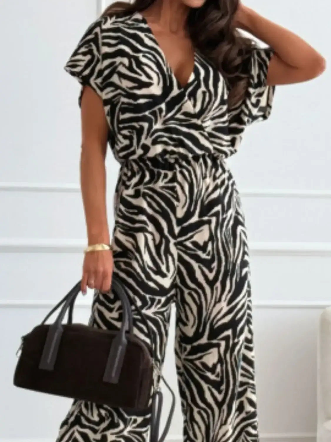 Woman wearing black and white zebra print jumpsuit holding a black handbag with gold bracelet