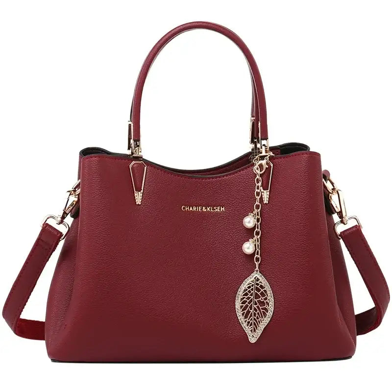 Burgundy leather handbag with gold hardware, top handles, shoulder strap, and leaf charm