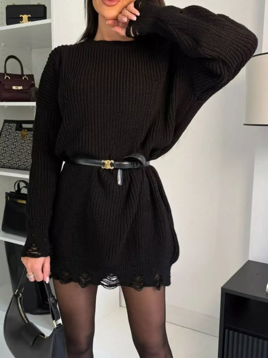 Woman wearing a black oversized knit sweater dress with a black belt and black tights.