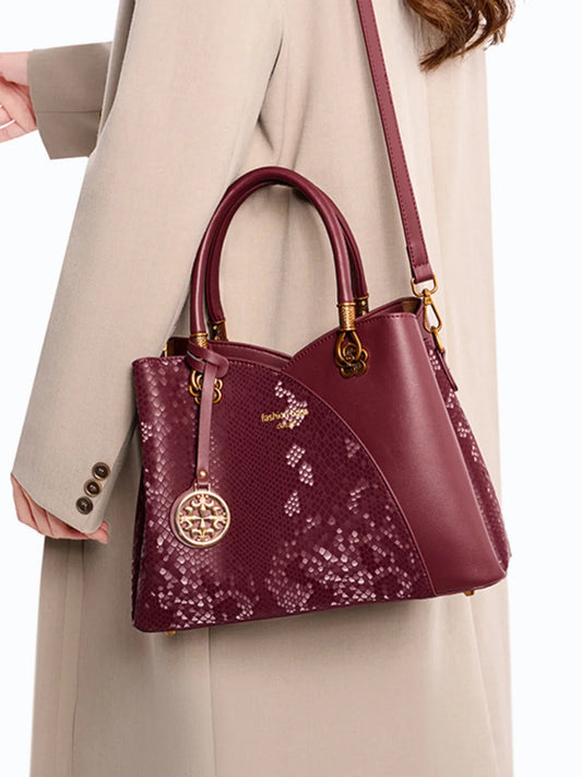 Burgundy snakeskin-patterned handbag with gold hardware, worn over a beige coat