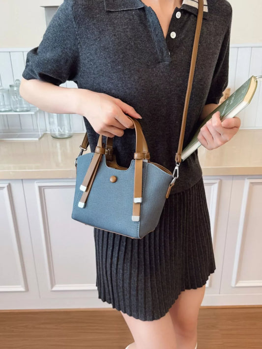 Woman in dark grey dress holding a small blue handbag with brown straps and a green book indoors