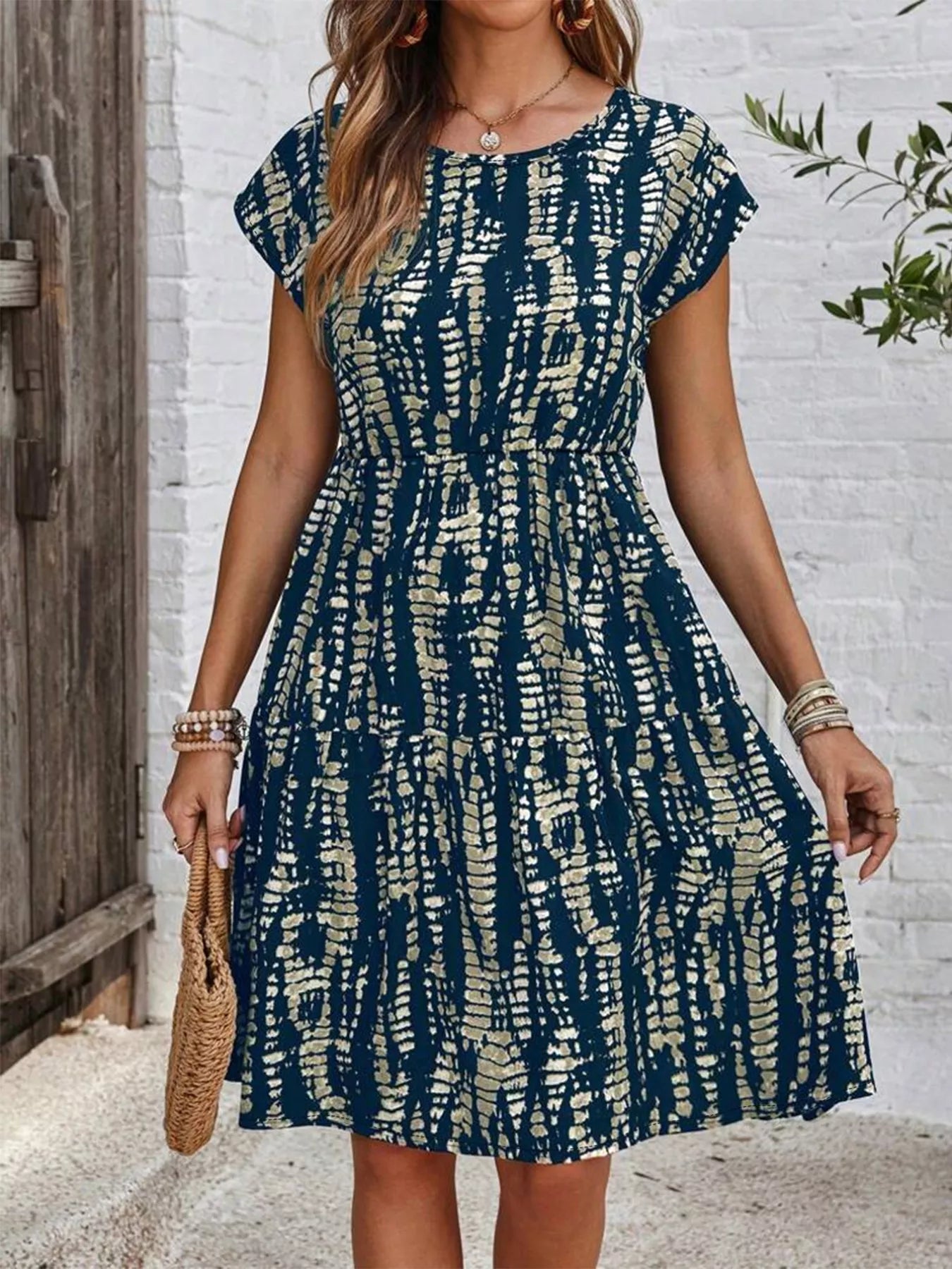 Woman wearing a navy blue and cream abstract printed casual short-sleeve dress holding a woven handbag outdoors
