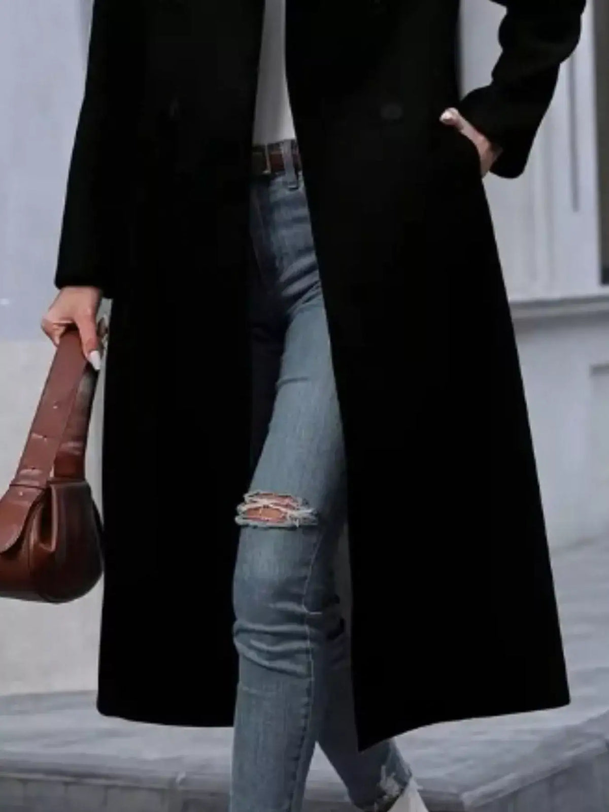 Woman wearing a black longline double-breasted overcoat by Evie's Dreamland, styled with ripped blue jeans.