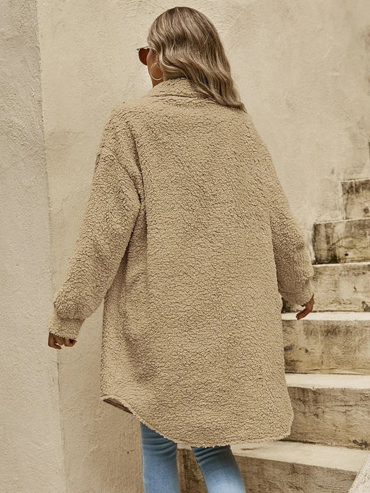 Back view of a woman wearing a long tan teddy fleece coat and blue jeans.
