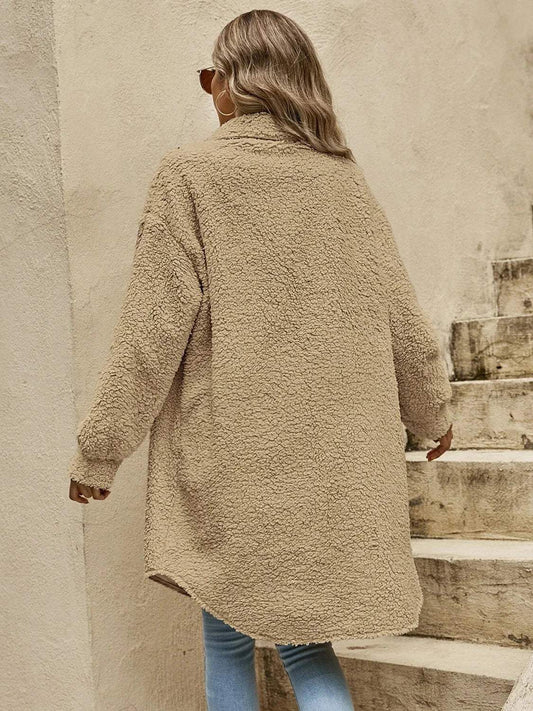Back view of a woman wearing a long tan teddy fleece coat and blue jeans.