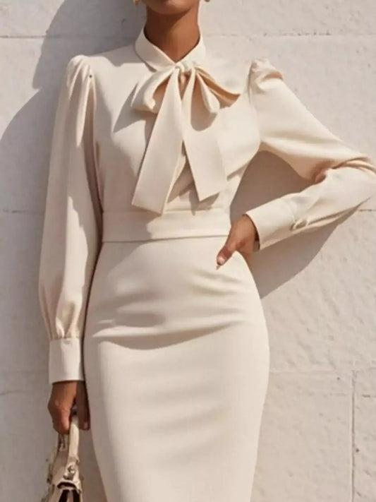 Woman wearing elegant cream long sleeve dress with bow tie neck detail, standing outdoors