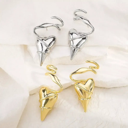 Gold and silver heart-shaped spike earrings with twisted wire design on white fabric