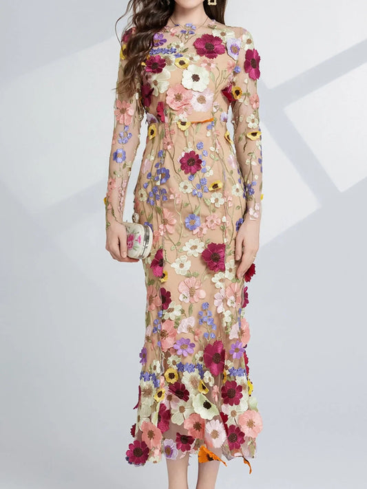 Woman wearing a sheer nude midi dress with colorful floral embroidery, holding a clutch.
