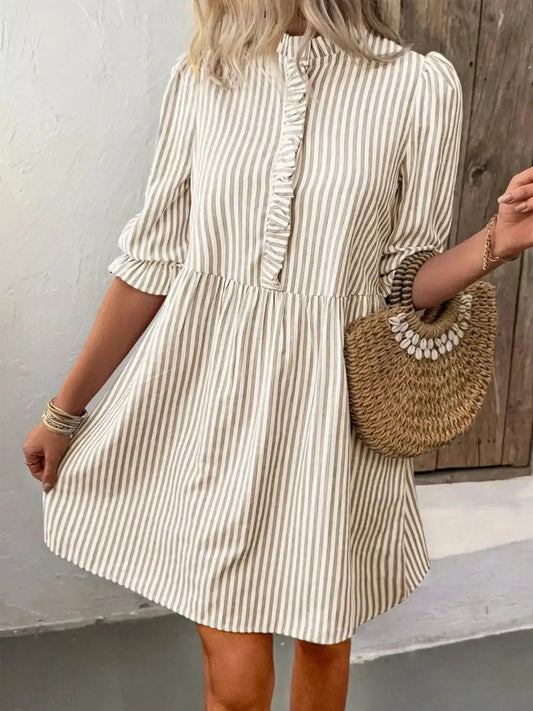 Woman wearing a striped half sleeve dress with frill details and buttoned front, made of viscose blend fabric