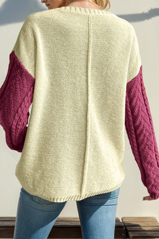 Back view of a woman wearing a cream knit sweater with magenta cable-knit sleeves and blue jeans.