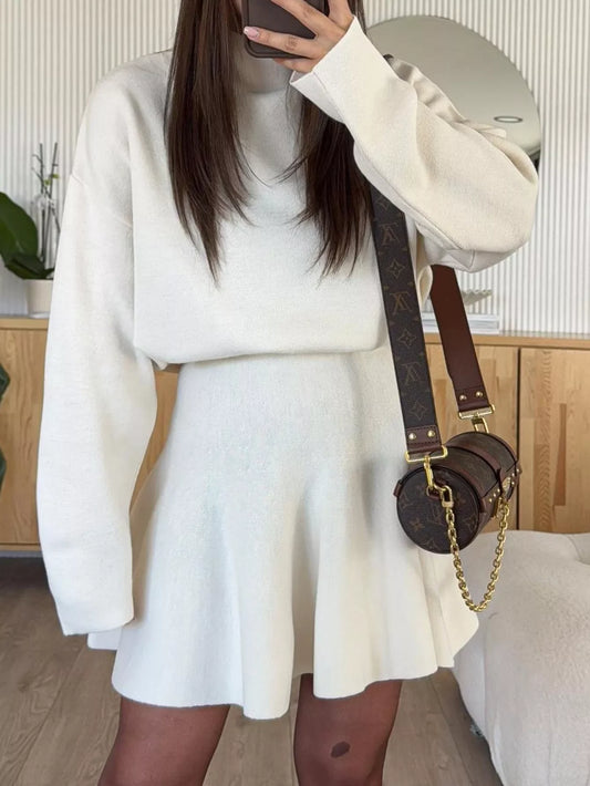 Woman wearing a white knit long sleeve top and matching flared mini skirt with a brown monogram bag