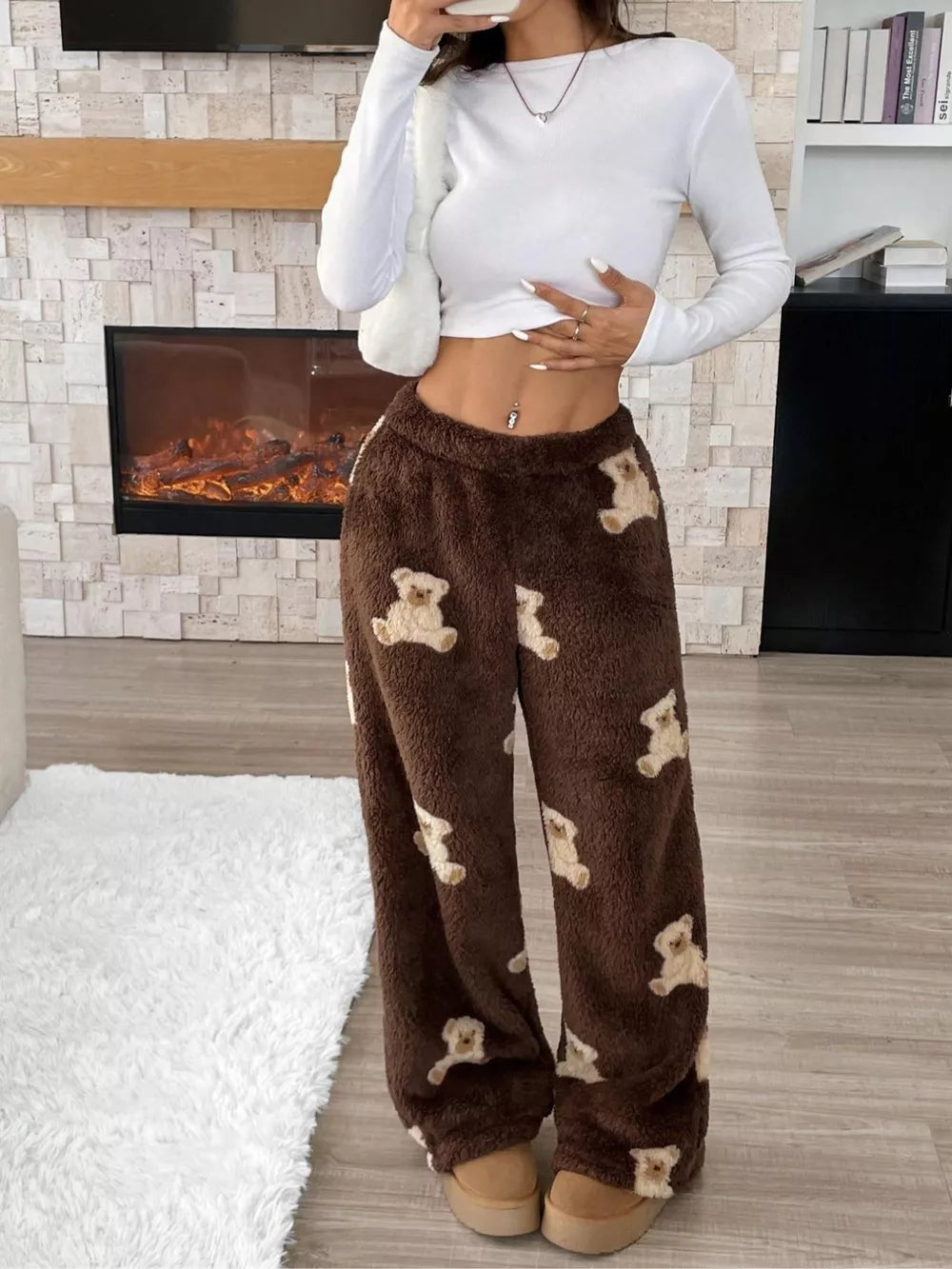 Woman wearing cozy brown teddy bear print fleece pants and a white cropped long sleeve top indoors