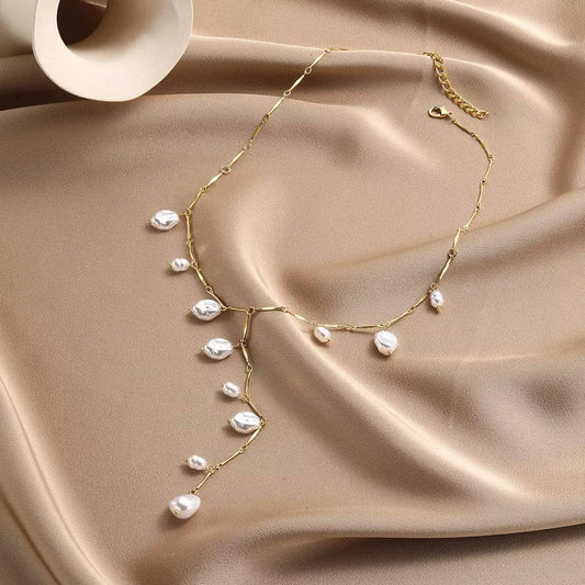 Elegant gold chain necklace with baroque pearls, styled on soft beige fabric for everyday chic fashion.