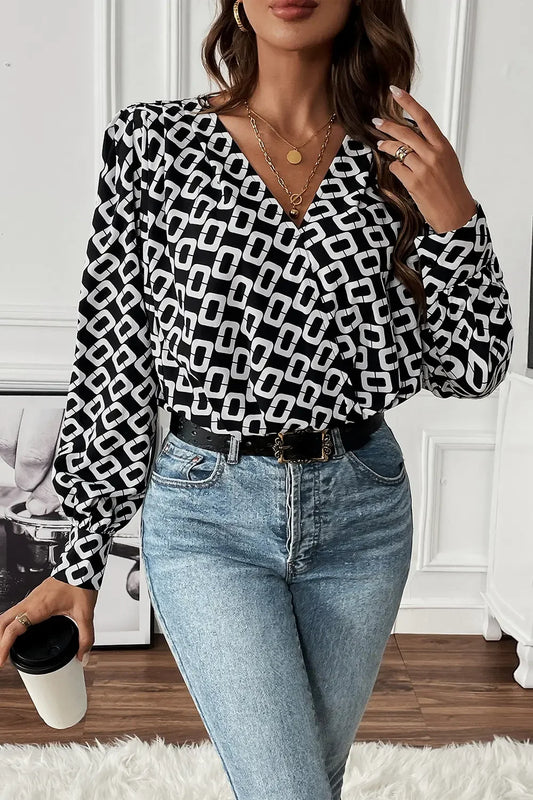 Woman wearing black and white geometric patterned blouse with puff sleeves and light blue high-waisted jeans holding coffee cup