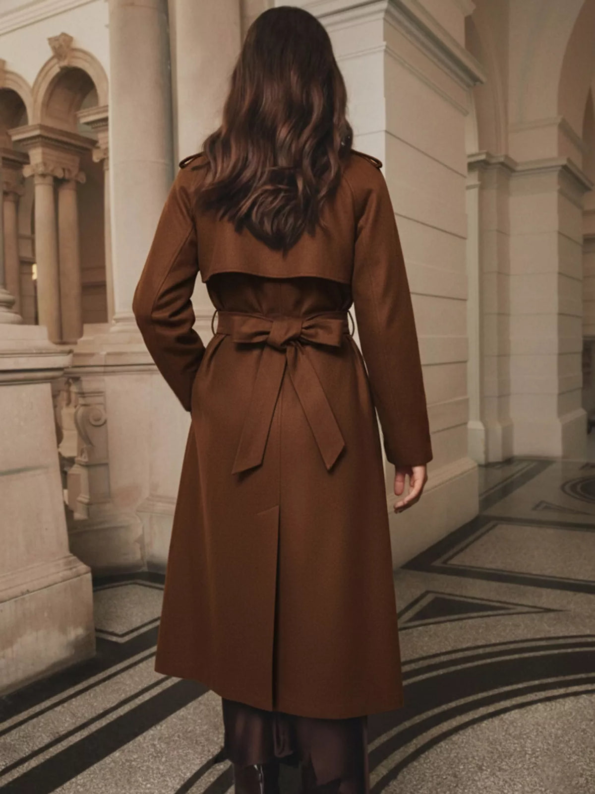 Back view of brown lapel collar belted wool blend coat showing tie waist bow and pleated hem detail