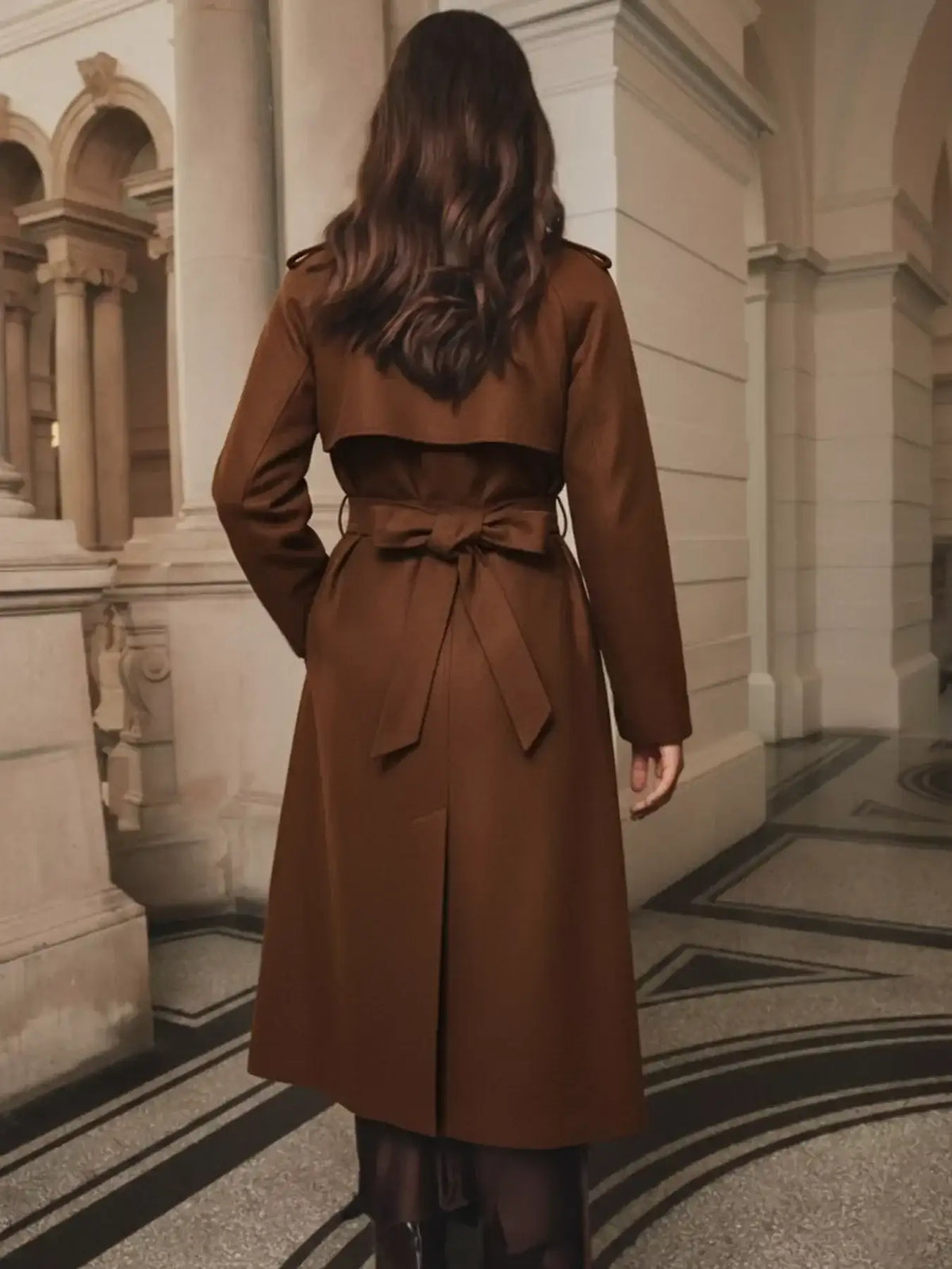 Back view of brown lapel collar belted wool blend coat showing tie waist bow and pleated hem detail