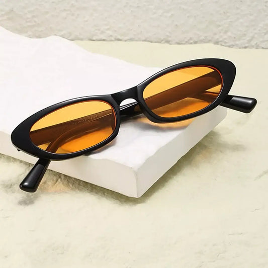 Black oval sunglasses with orange tinted lenses resting on a white textured surface.