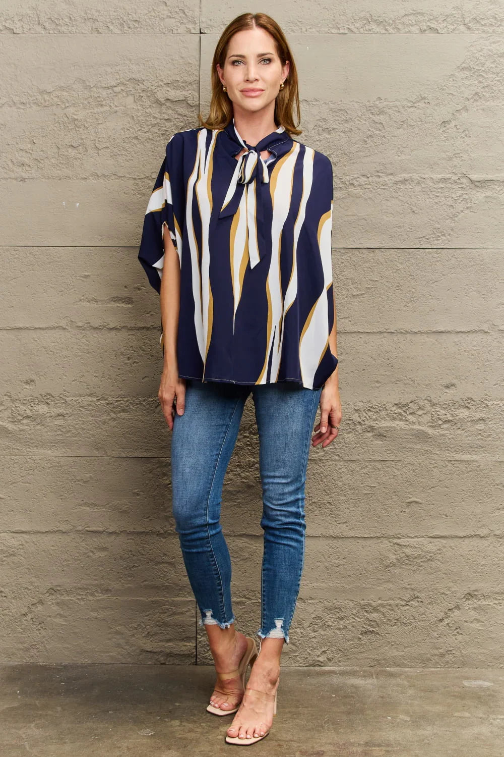 Woman wearing a navy striped blouse with bow tie and distressed blue skinny jeans