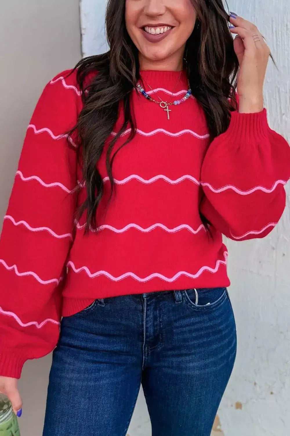 Woman wearing an Evie's Dreamland red round neck pullover sweater with pink wavy stripes and puff sleeves.