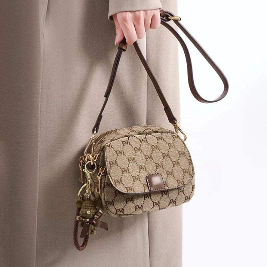 Woman holding a stylish beige crossbody bag with brown monogram print and bear keychain