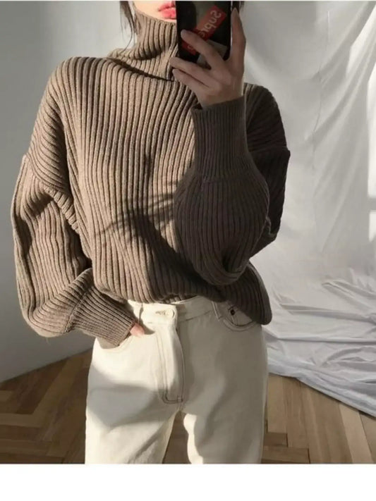 Woman wearing a brown ribbed turtleneck oversized sweater and white trousers.