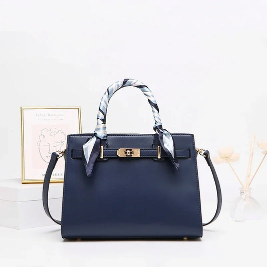Navy blue structured handbag with gold hardware and silk scarf handles on white table