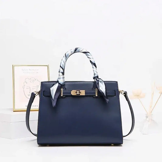 Navy blue structured handbag with gold hardware and silk scarf handles on white table