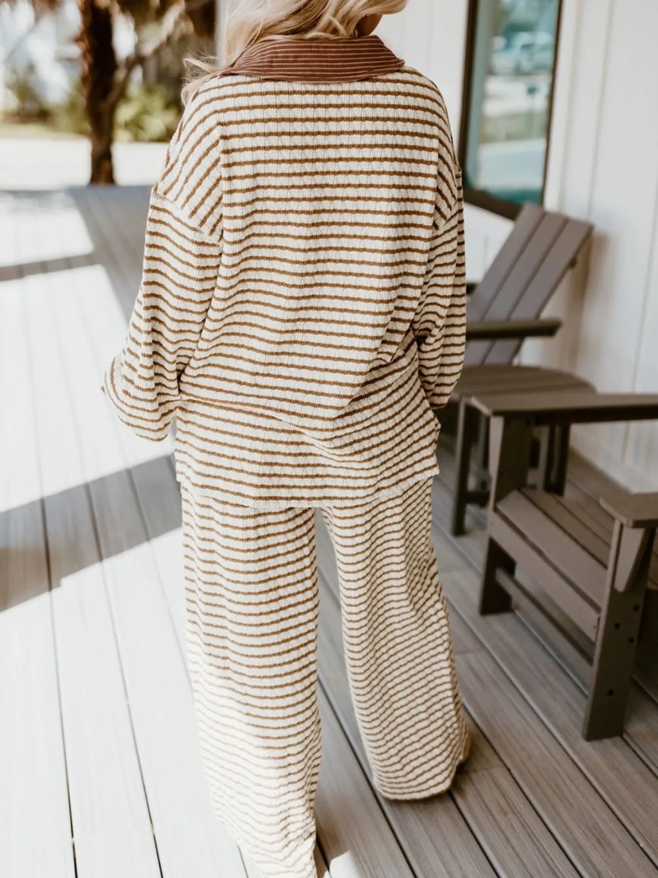 Woman wearing cozy beige and white striped loungewear set standing on a wooden porch near chairs