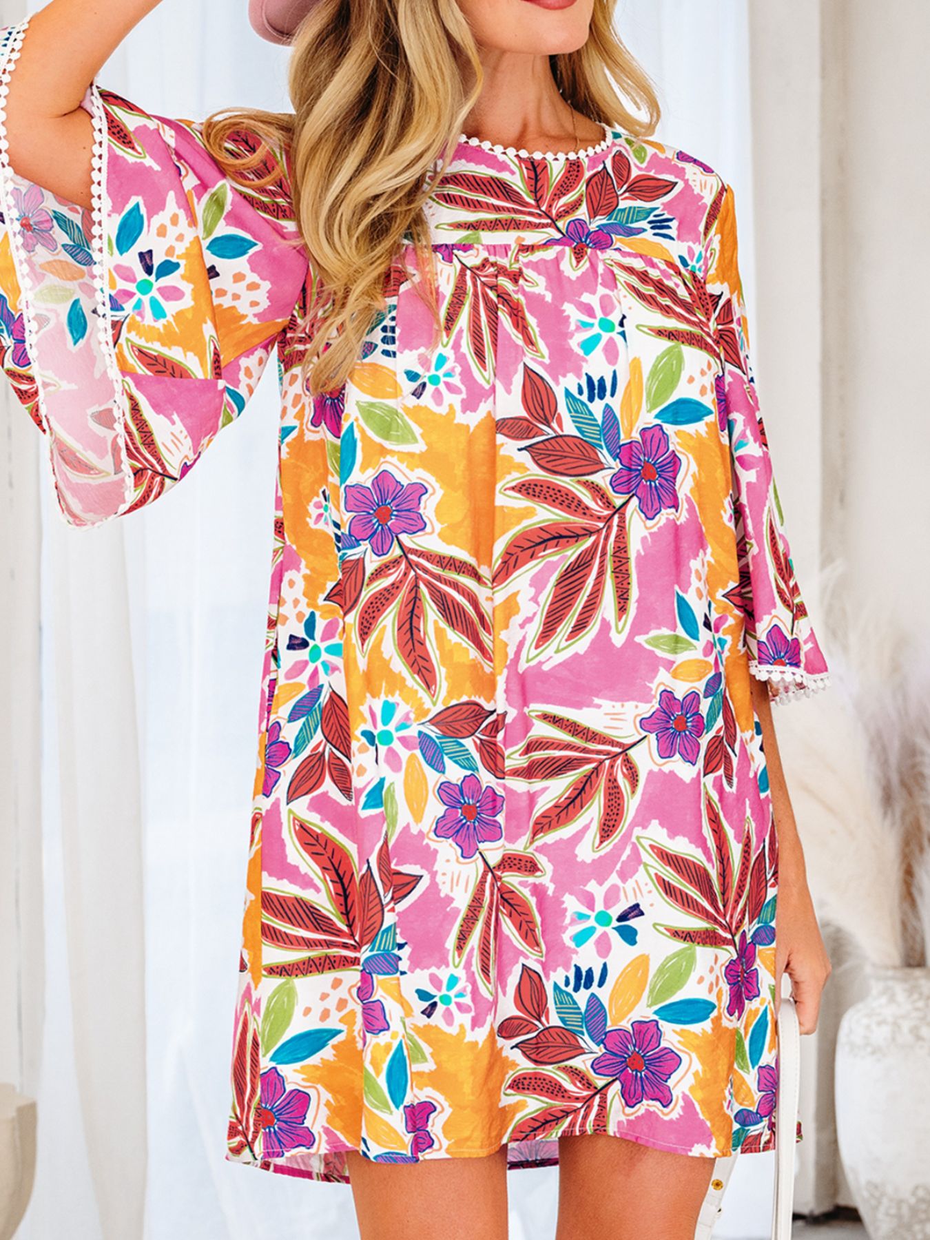 Woman wearing a colorful floral print dress with flared sleeves and white trim detail