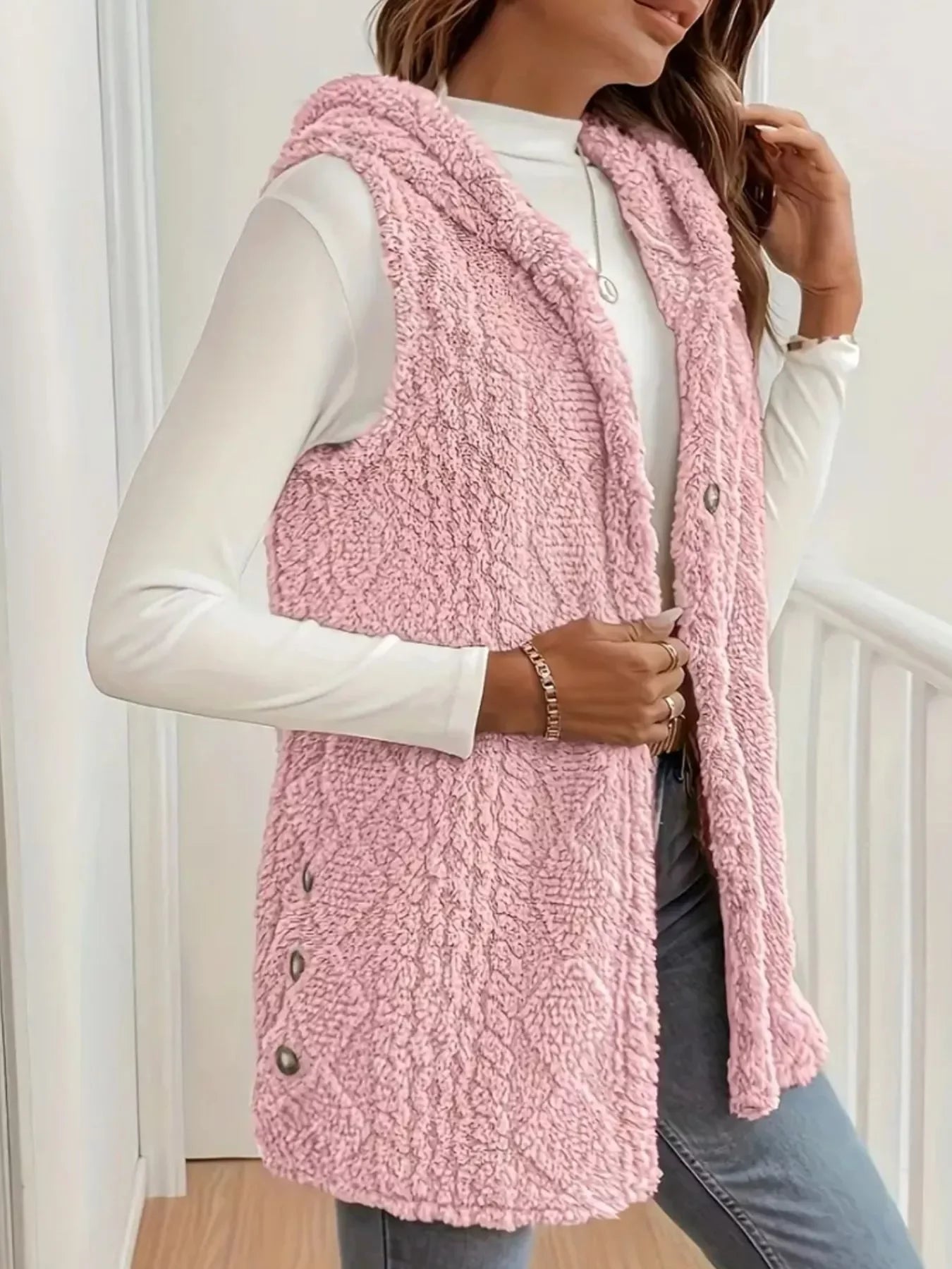 Woman wearing pink sherpa fleece sleeveless vest with buttons, white long-sleeve top, and jeans