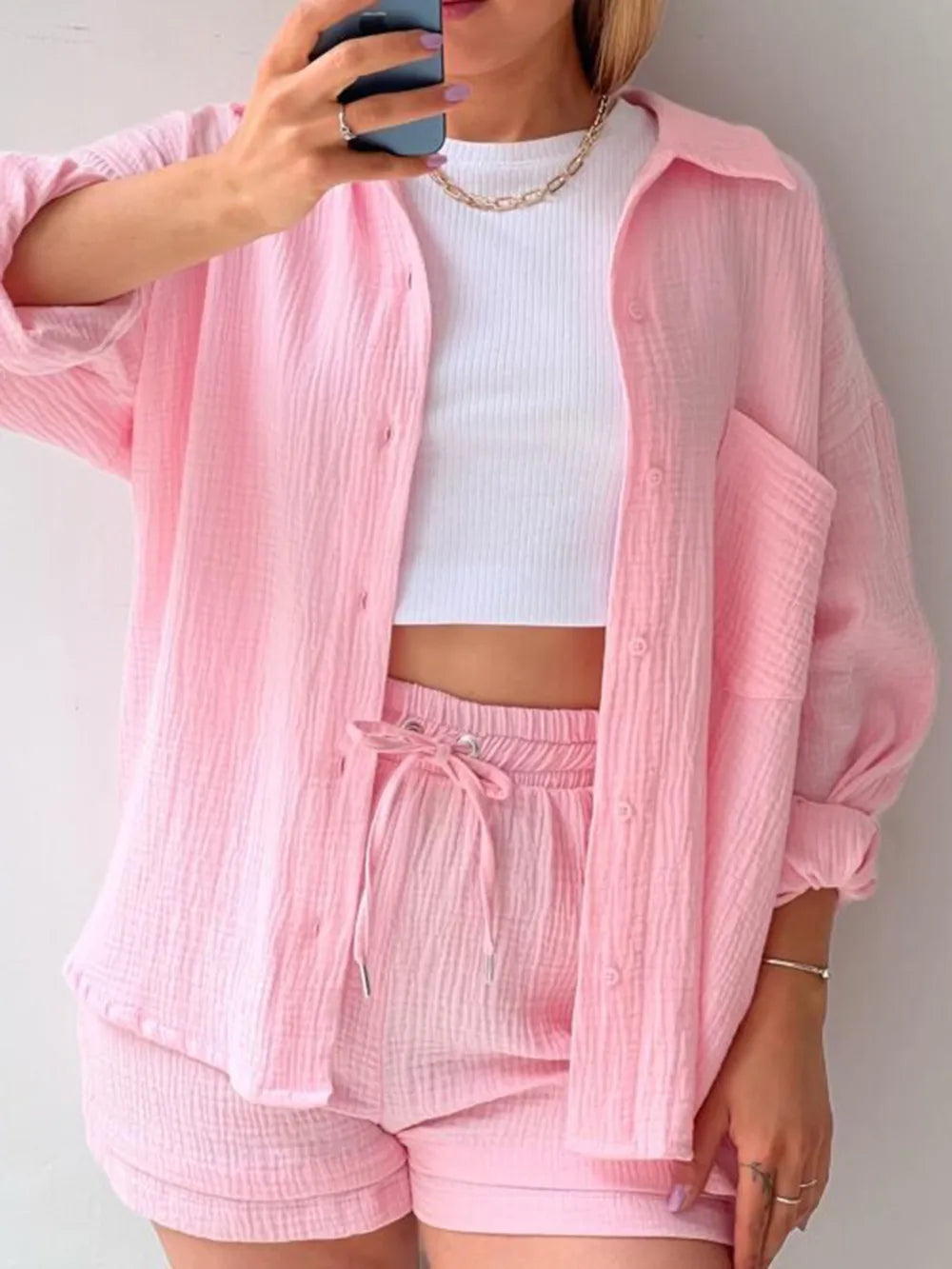 Woman wearing a pink button-up lounge set with shorts and a white ribbed crop top