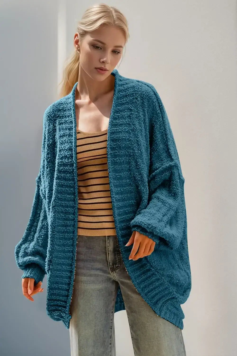 Woman wearing cozy teal oversized cardigan, striped tank top, and casual jeans
