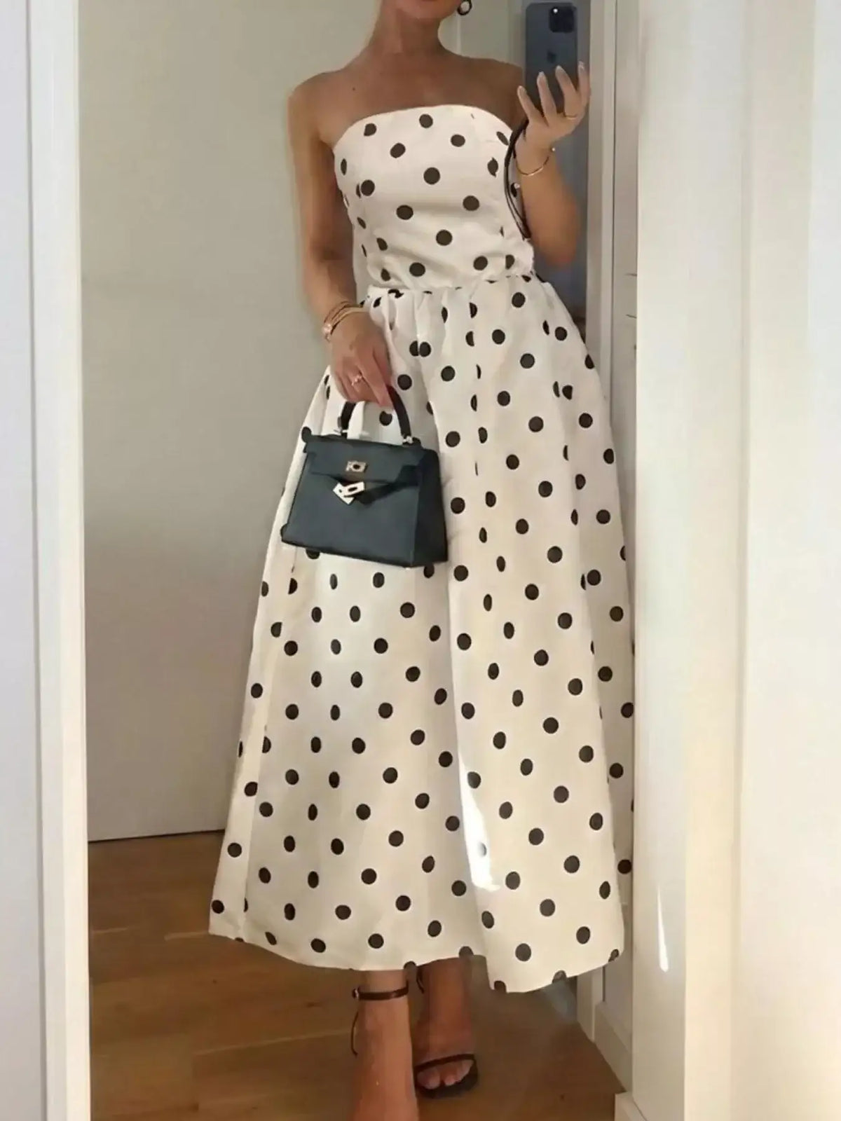 Woman wearing an Evie's Dreamland strapless white midi dress with black polka dots and a black handbag.