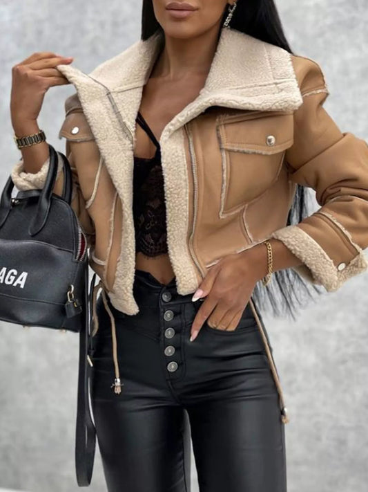 Woman wearing tan shearling jacket with black lace top and high-waisted black leather pants, holding black designer handbag
