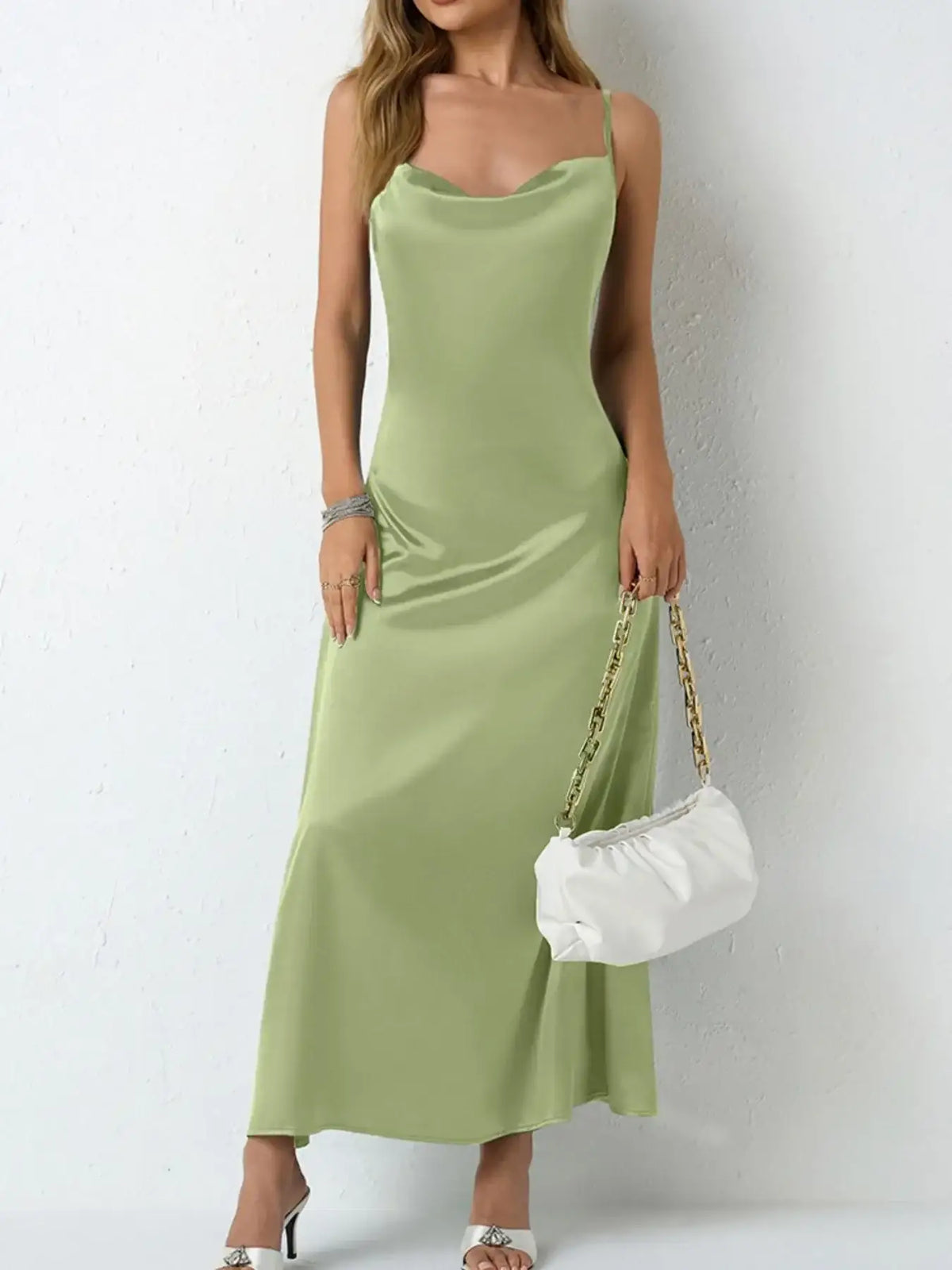 Woman wearing an Evie's Dreamland sage green satin cowl neck slip maxi dress with a white handbag.