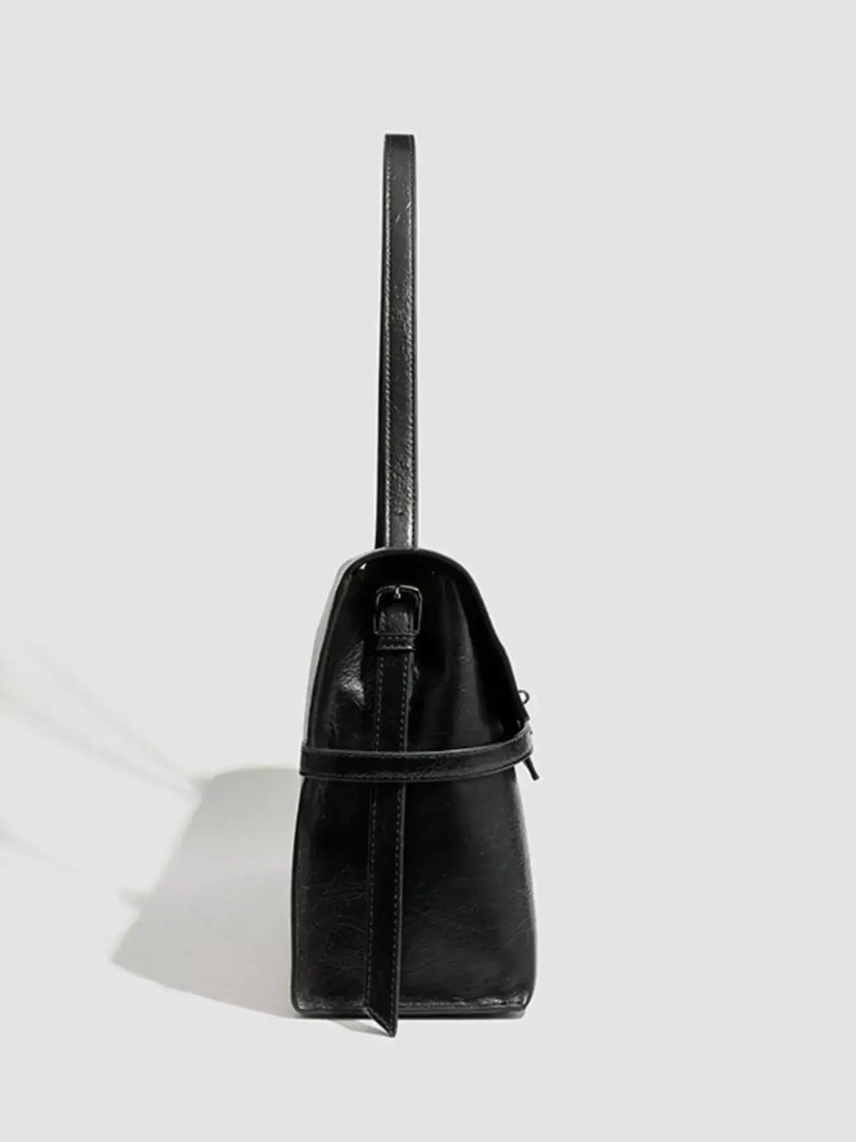 Side view of a black Evie's Dreamland medium PU leather shoulder bag with buckle strap detail.