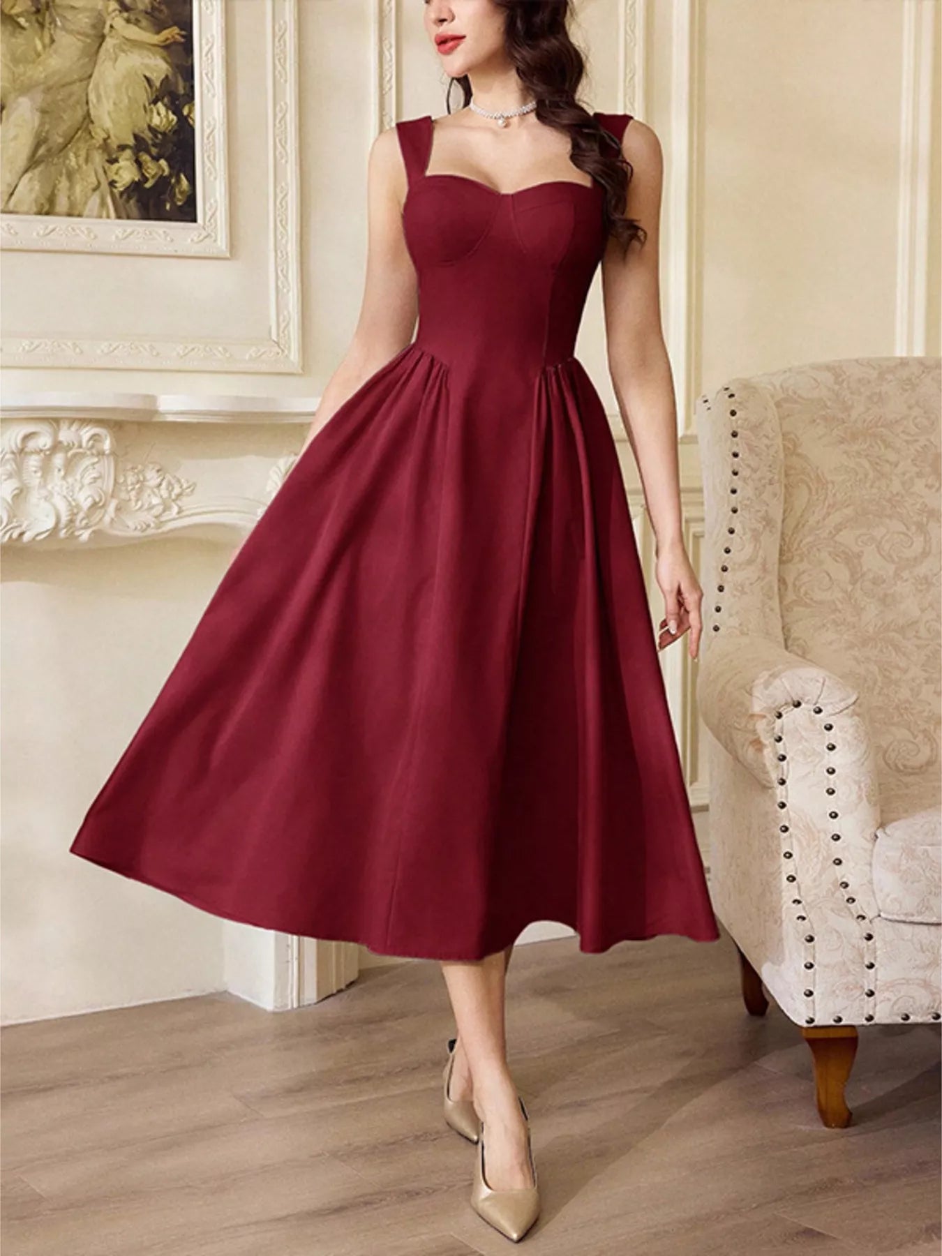 Woman wearing a burgundy sleeveless midi dress with a flared skirt and gold heels.