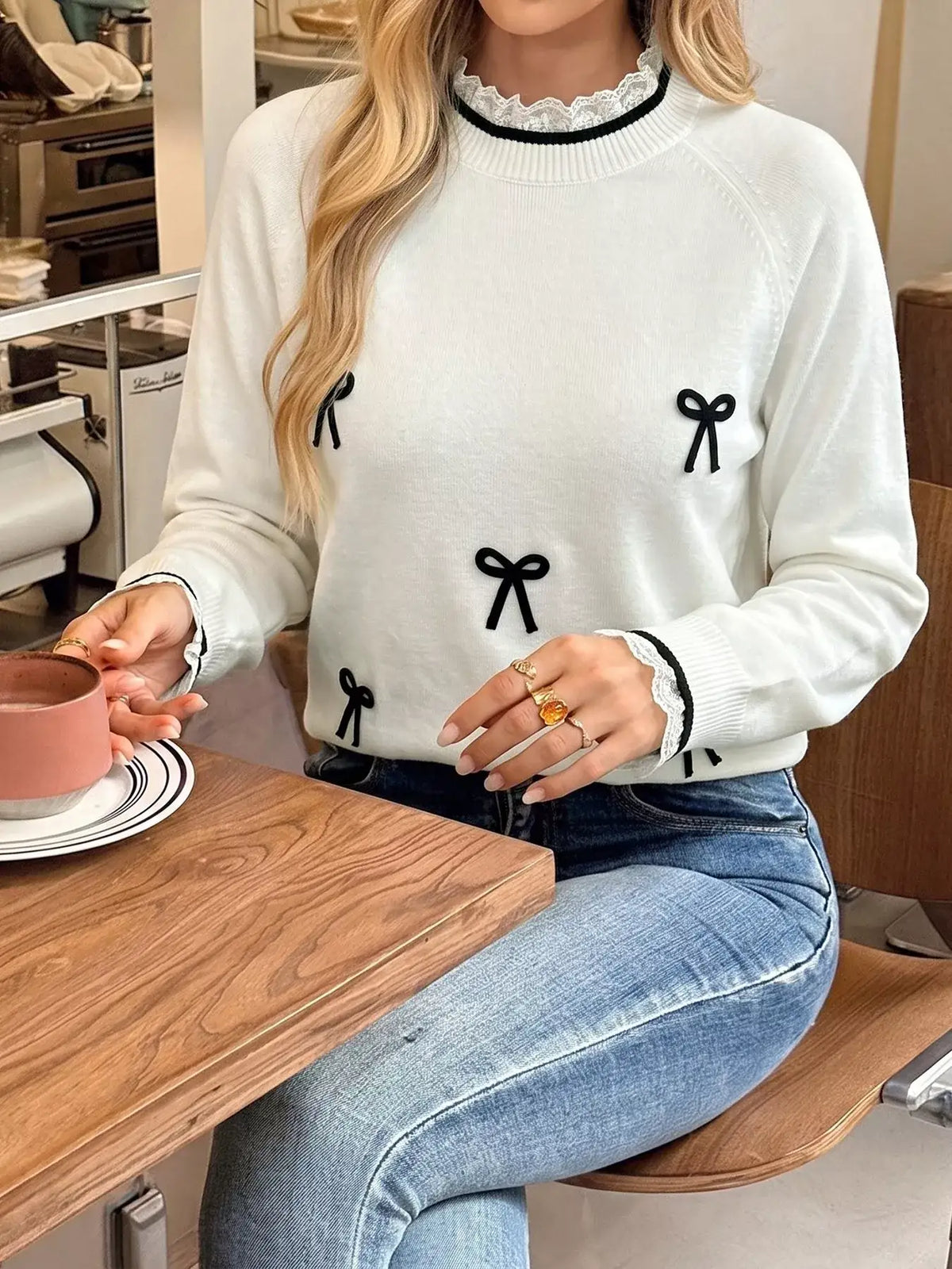 Woman wearing a white Evie's Dreamland bow-embellished sweater with lace trim and blue jeans.