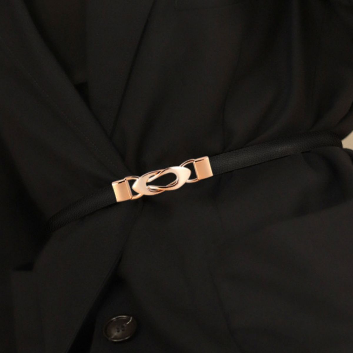 Close-up of a black garment with a thin black belt and a rose gold buckle