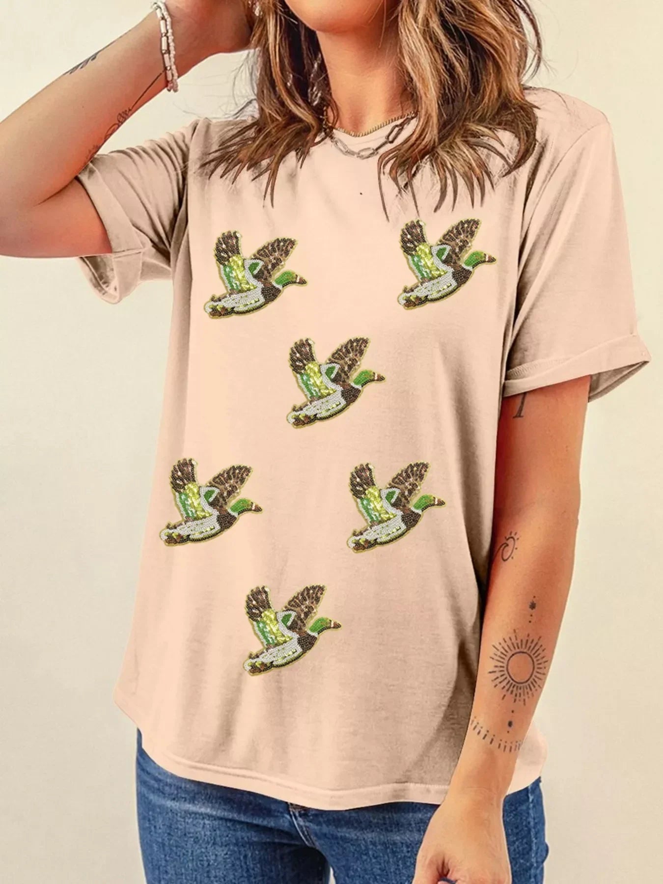 Woman wearing beige t-shirt with six flying duck embroidery designs, casual outfit with jeans