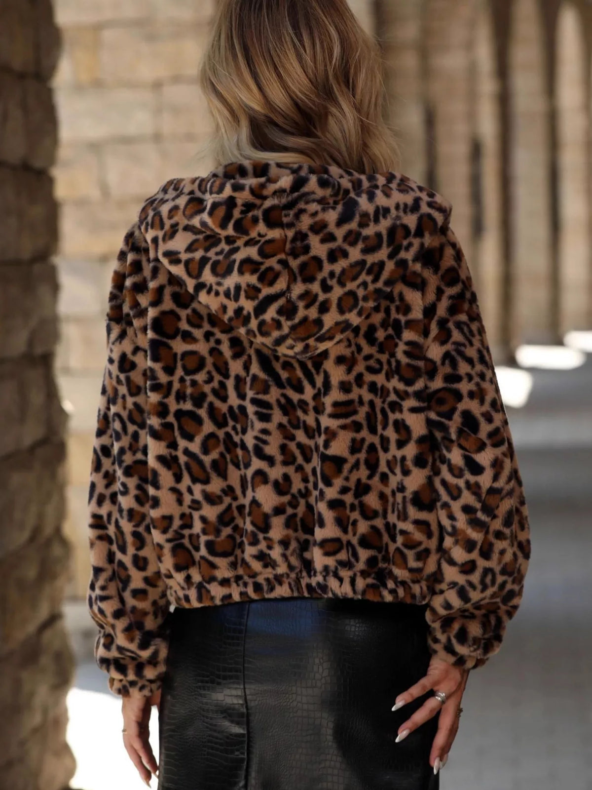 Back view of a woman wearing an Evie's Dreamland leopard print faux fur hooded jacket and black leather skirt.