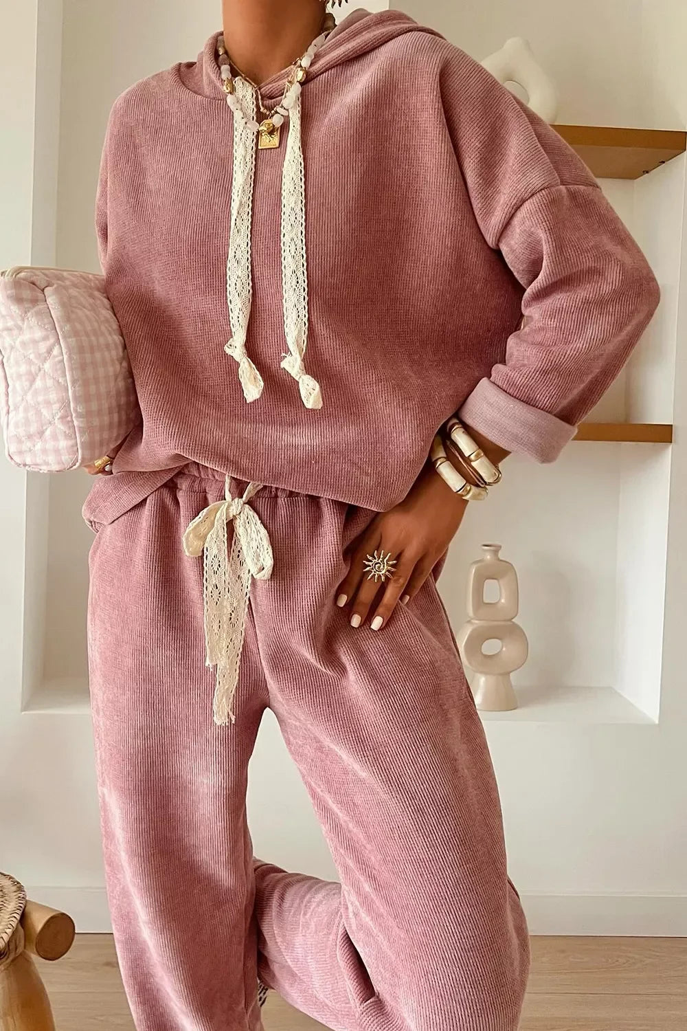Woman wearing a pink corduroy lounge set with lace details, holding a plaid clutch bag