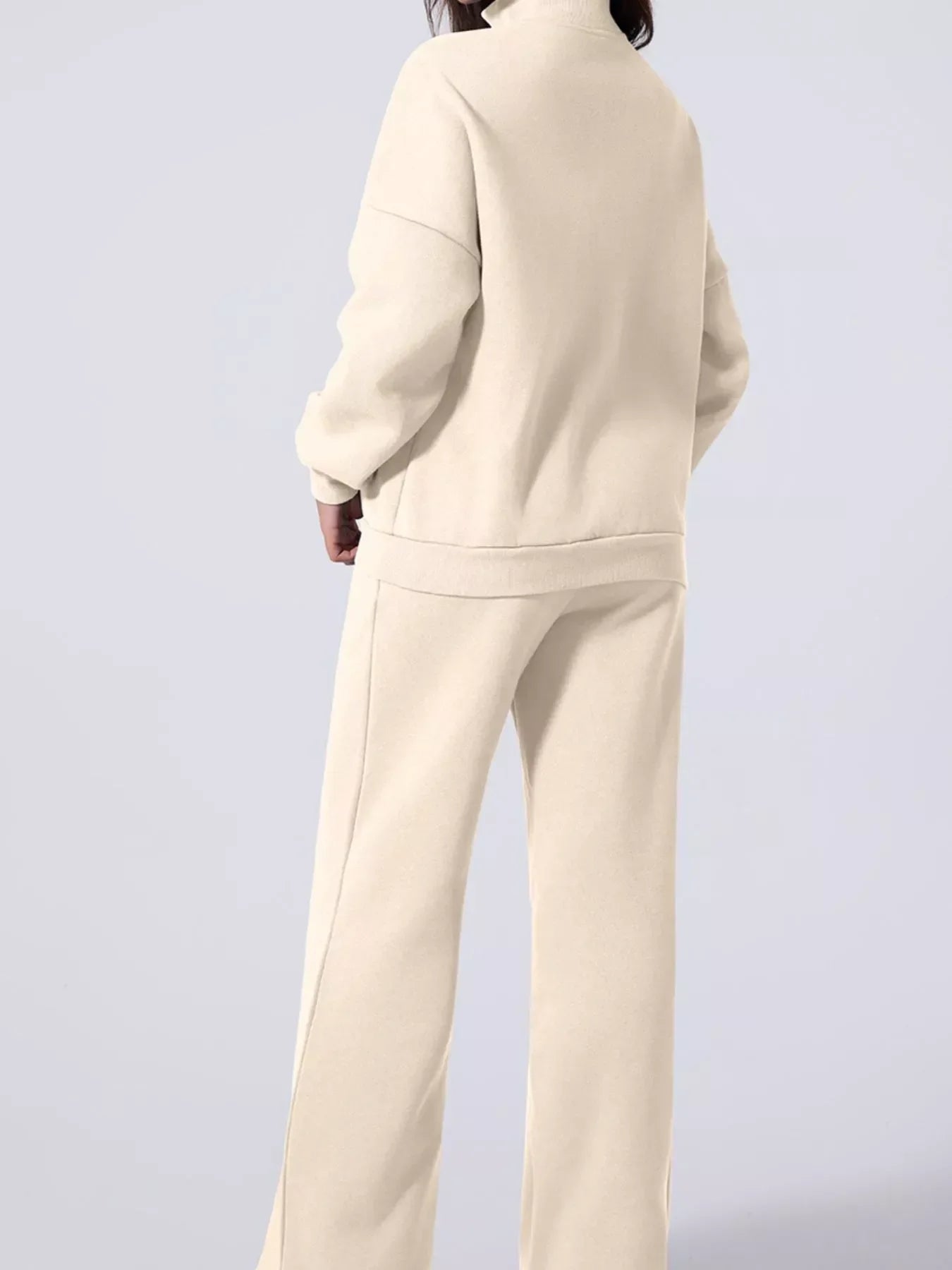 Back view of model wearing beige cozy high-neck sweatshirt and wide-leg sweatpants loungewear set